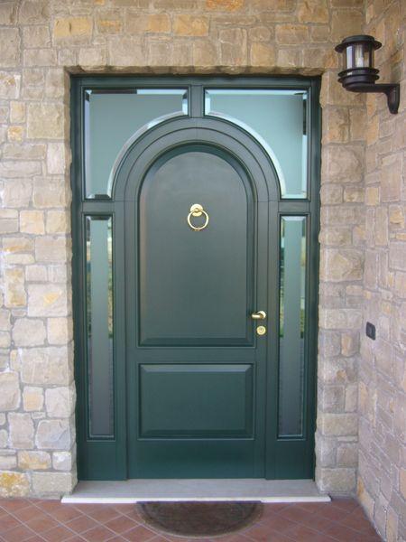 Porta d'ingresso verde scuro in stile classico, incorniciata da mura in pietra, maniglia dorata e timpano arrotondato.