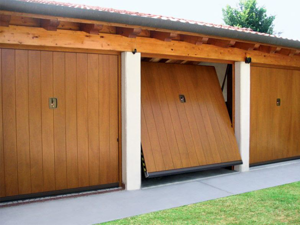 Due porte garage in legno scorrevoli, una leggermente aperta, su una struttura coperta, con prato verde sullo sfondo.
