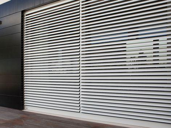 Facciata con tende metalliche a sbarre orizzontali, chiude una vetrata carrabile; atmosfera urbana minimalista.